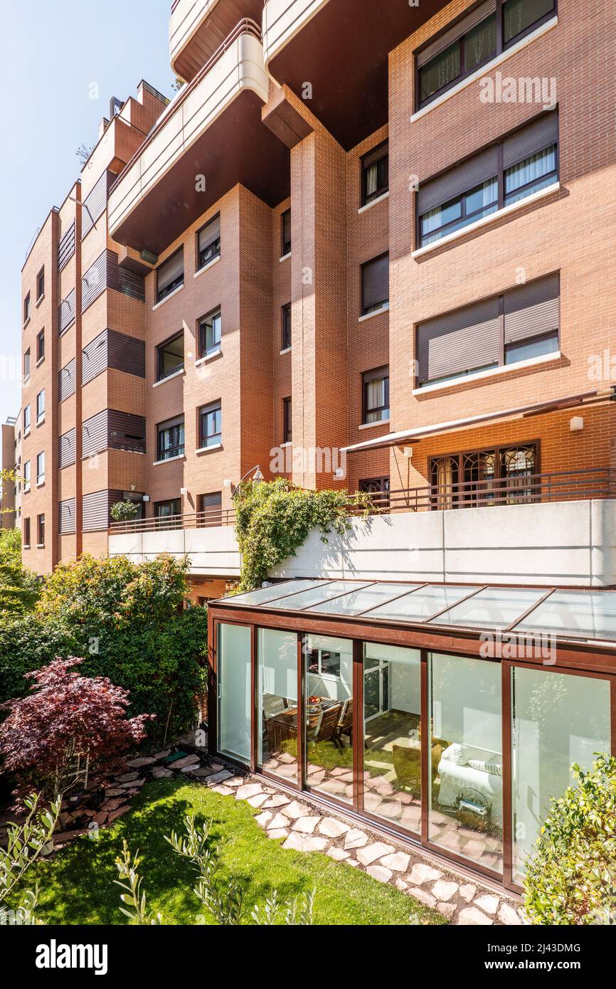 Terrasse couverte avec structure en aluminium marron et verre avec accès à l'appartement au rez-de-chaussée d'un immeuble résidentiel avec un ga Banque D'Images