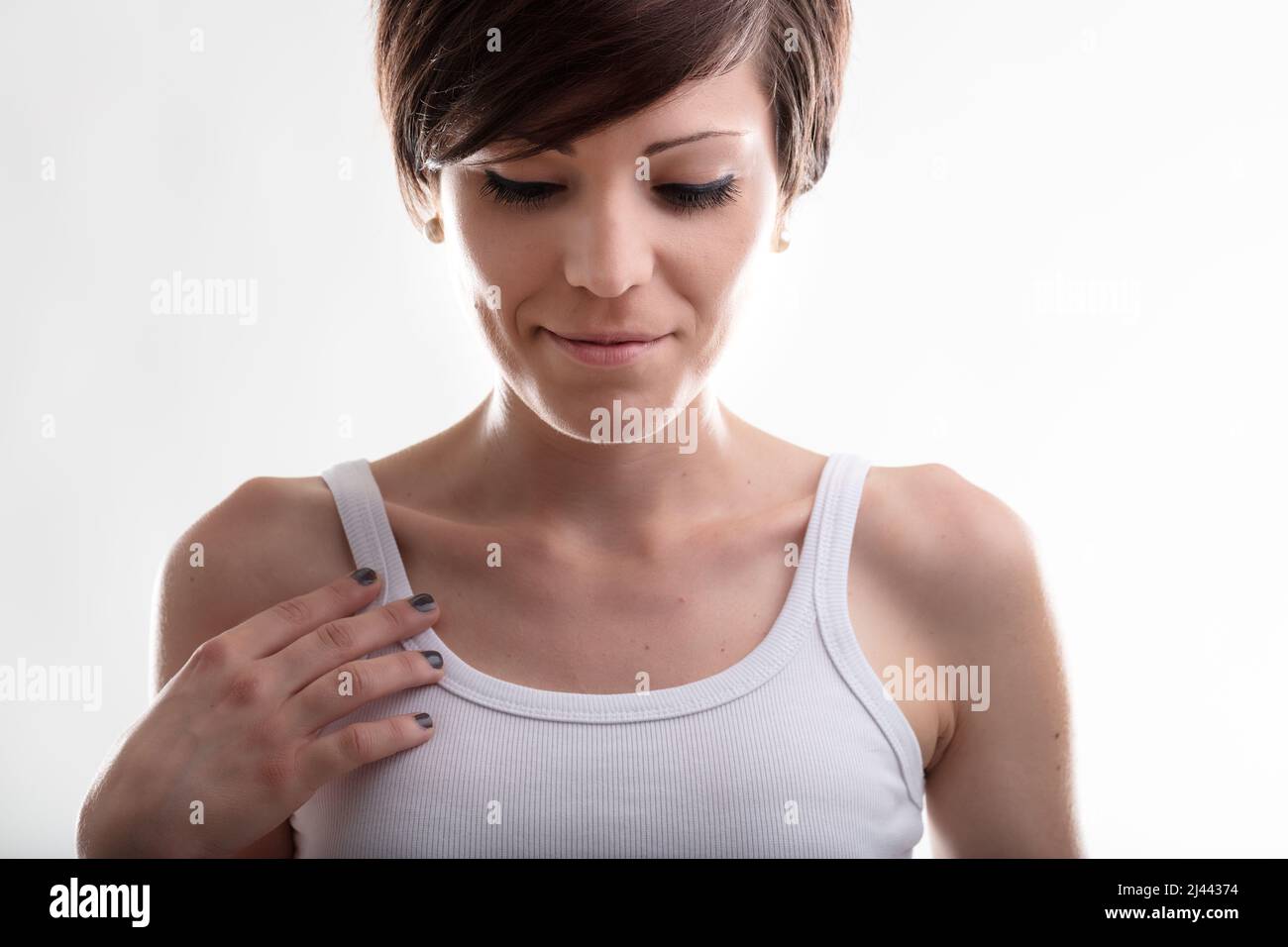 Demure jeune femme avec sa main à sa poitrine regardant vers le bas avec les yeux en duvet et un sourire tranquille dans un petit gros plan Banque D'Images