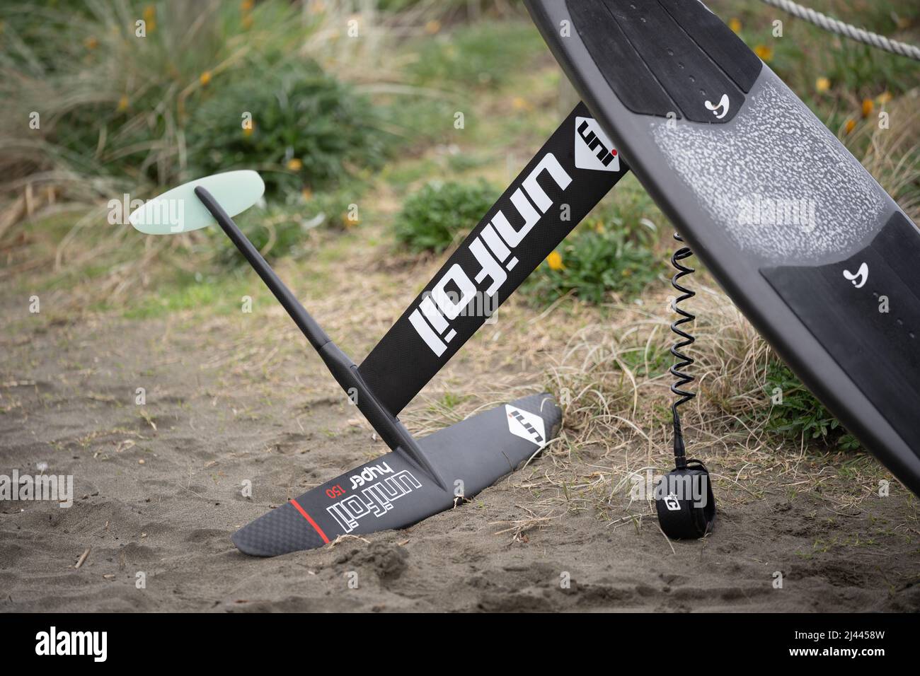 Une planche de surf hydrofoil en fibre de carbone avec hydrofoil en fibre de carbone et laisse se trouve sur le sable à Piha Beach, Auckland, Nouvelle-Zélande. Banque D'Images