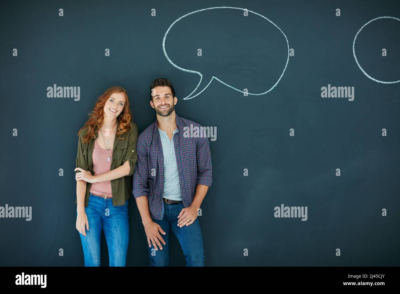 Elle aime un homme qui parle son esprit. Portrait d'un jeune couple debout devant un tableau noir avec des bulles de parole dessinées dessus. Banque D'Images