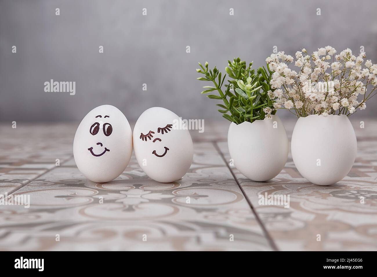 Composition de Pâques. Œufs blancs aux visages amusants peints sur la table. Un petit bouquet dans un œuf. Le concept minimal de Pâques. Une carte de Pâques avec un Banque D'Images