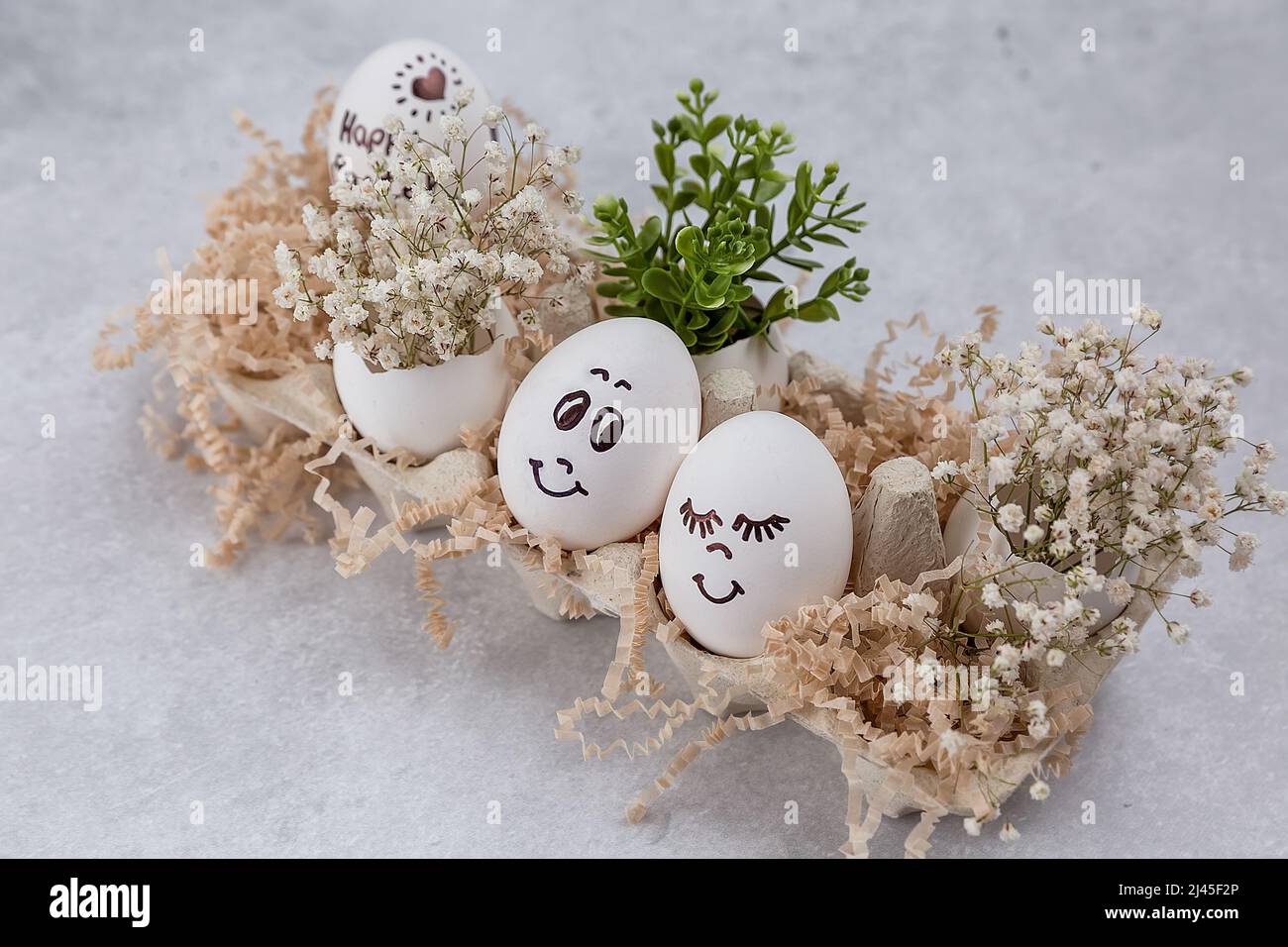 Composition de Pâques. Œufs blancs aux visages amusants peints sur la table. Un petit bouquet dans un œuf. Le concept minimal de Pâques. Une carte de Pâques avec un Banque D'Images