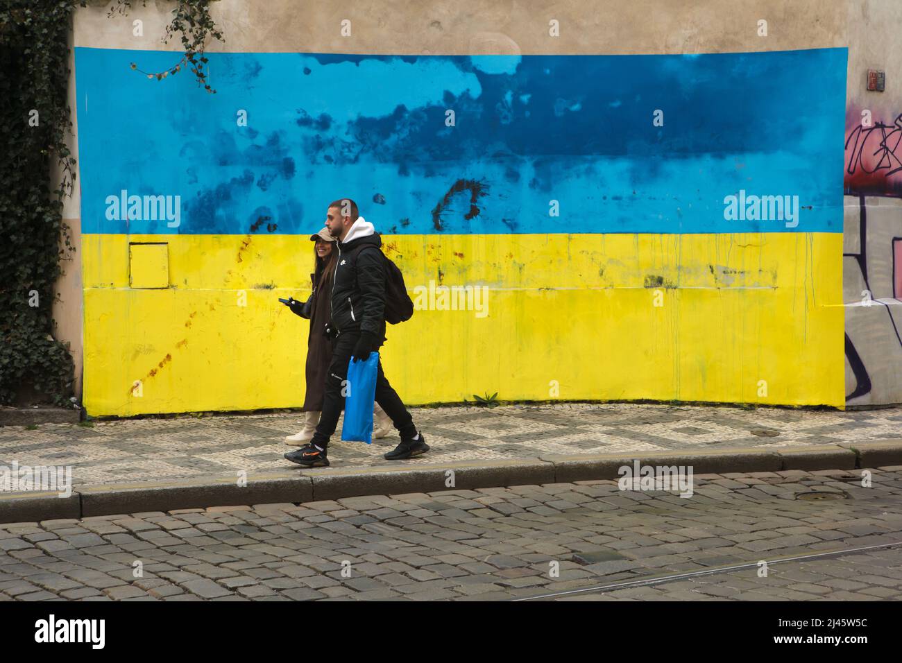 Les piétons passent par le drapeau national ukrainien représenté sur le mur de la rue Karmelitská à Malá Strana (ville de Lesser) à Prague, République Tchèque, photographié le 2 avril 2022. L'immense drapeau a été représenté dans le centre historique de Prague pour soutenir les réfugiés ukrainiens en République tchèque et pour protester contre l'invasion russe de l'Ukraine en 2022. Banque D'Images