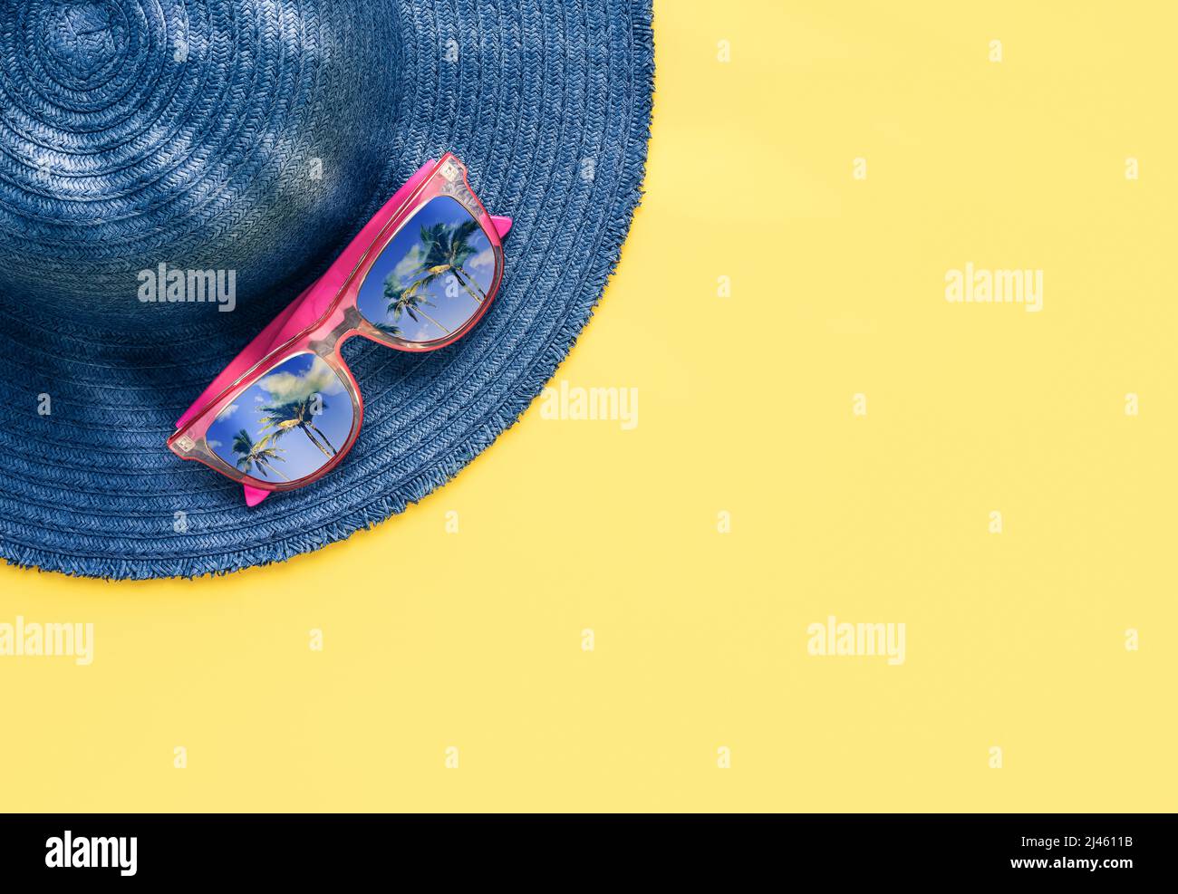 Concept de vacances d'été. Accessoires de plage, chapeau bleu et lunettes de soleil avec réflexion de palmier sur fond jaune. Vue de dessus, espace de copie Banque D'Images