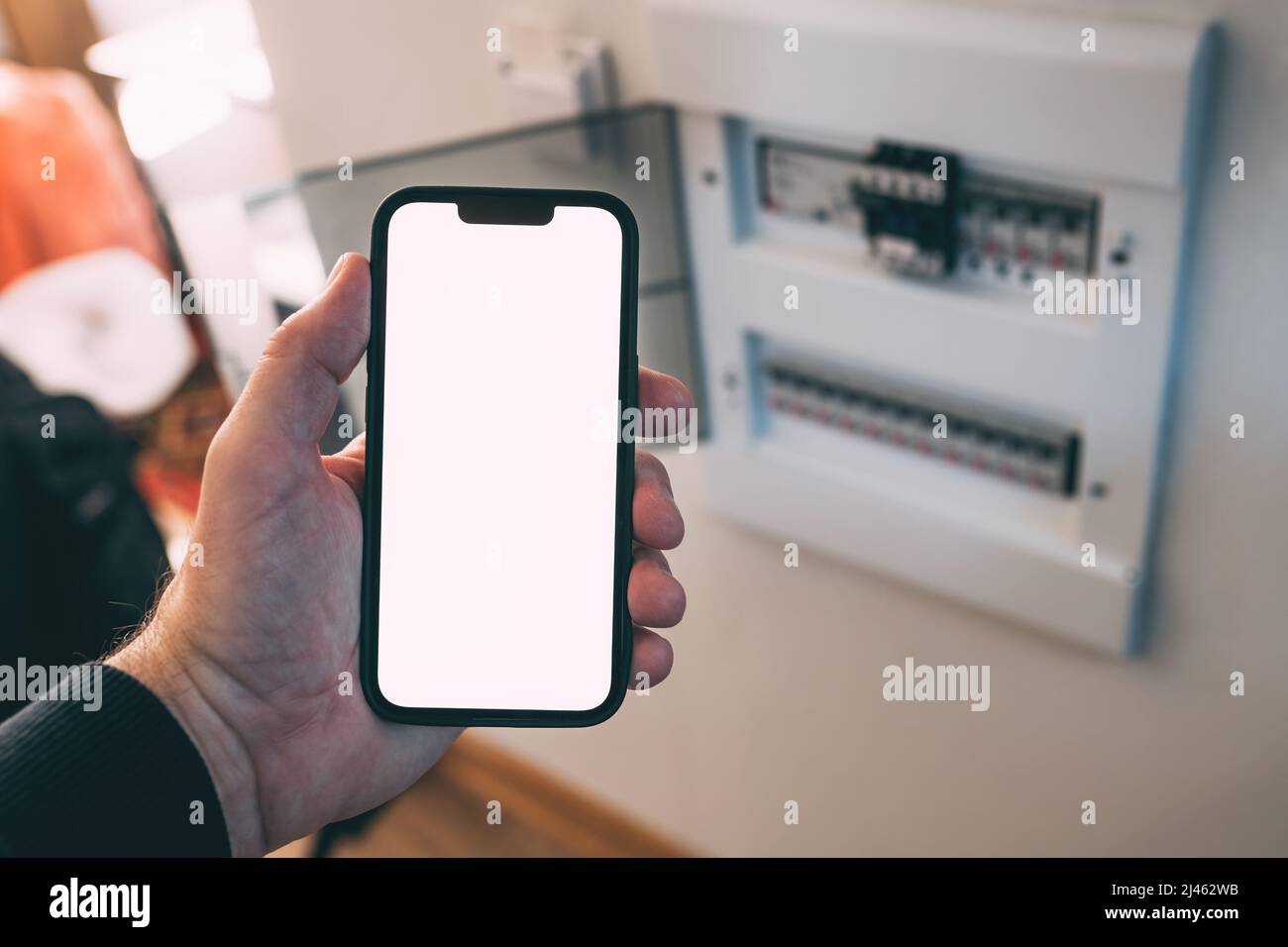 Électricien tenant un smartphone avec écran tactile maquette vierge devant le boîtier de disjoncteur à la maison, mise au point sélective Banque D'Images