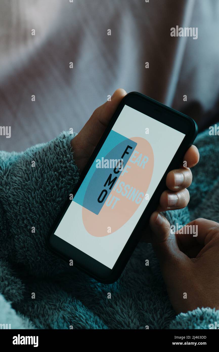 gros plan un homme, portant une confortable robe de maison grise, couché confortablement et en utilisant son smartphone, qui lit le texte fomo, par peur de manquer, dans son Banque D'Images
