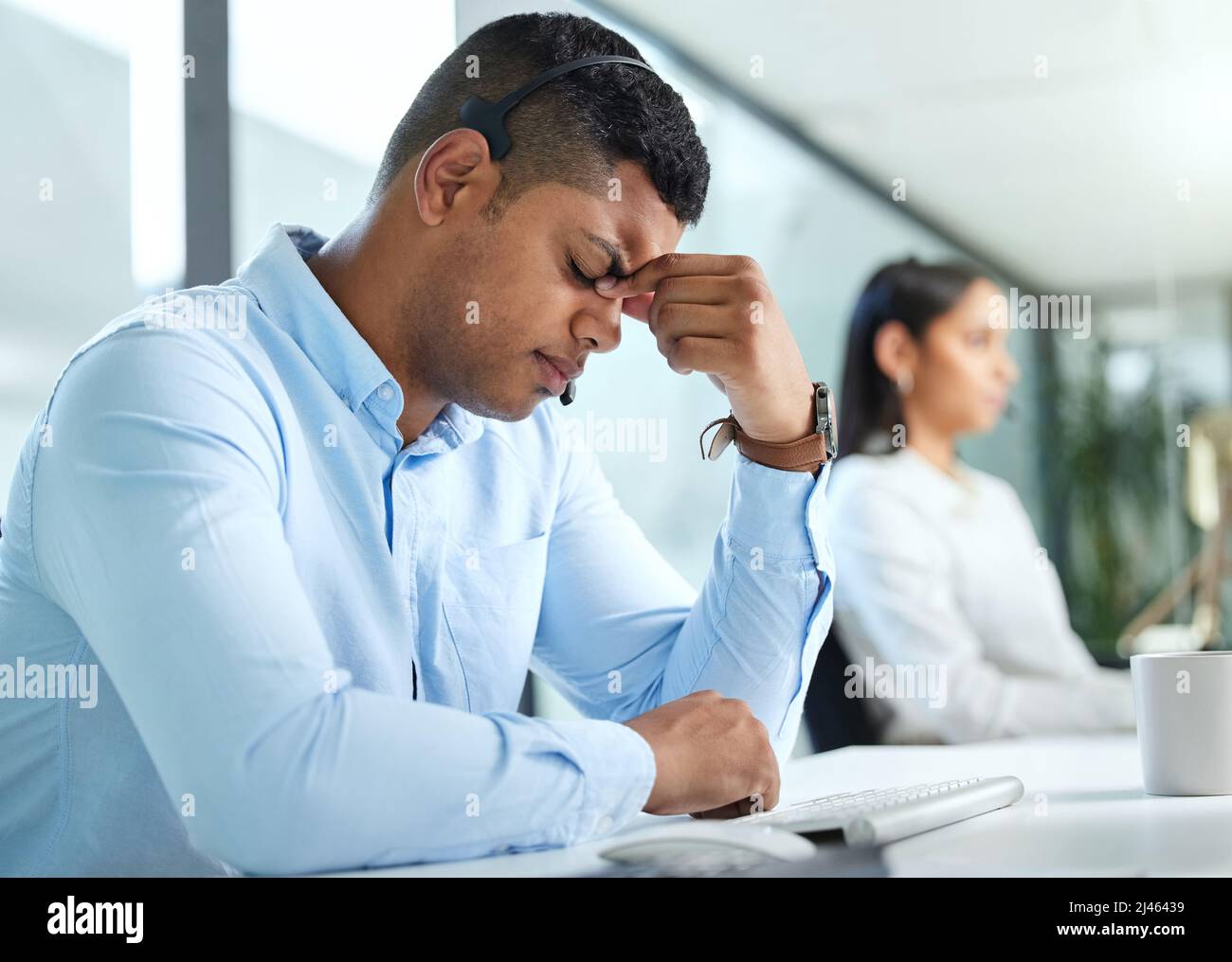 Ce client me donne un mal de tête. Photo d'un jeune agent de centre d'appels assis au bureau et souffrant de maux de tête tout en portant un casque. Banque D'Images