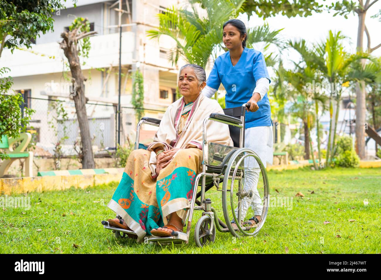Gros plan d'une infirmière qui a pris une femme âgée à pied en fauteuil roulant dans le jardin de l'hôpital - concept de gardien, d'invalidité et de soins de santé Banque D'Images