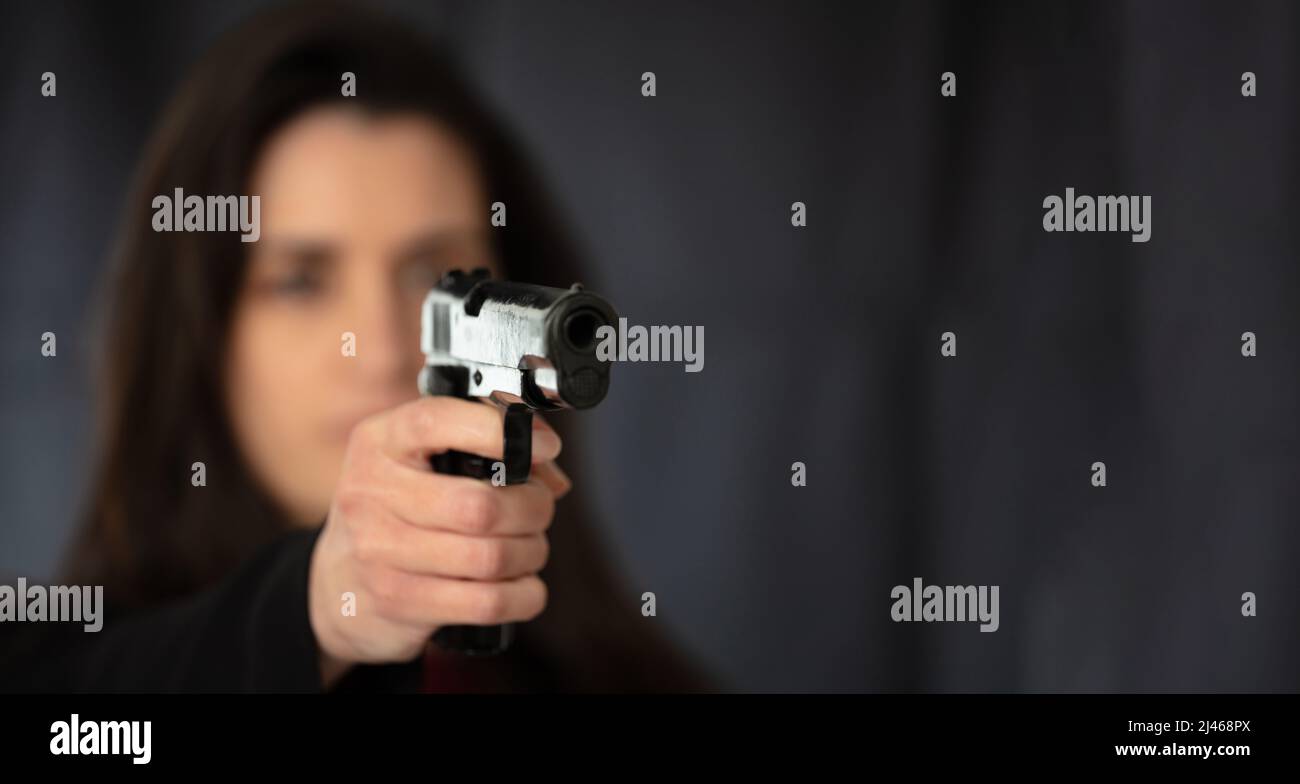 Femme tenant un pistolet dans la main pointant vers la caméra. Femme agent de police secrète, tueur ou espion cheveux longs dans fond sombre, espace de copie. Mise au point sélective Banque D'Images