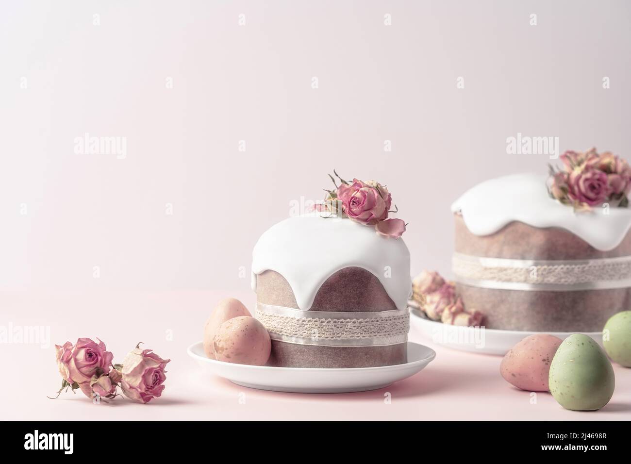 Gâteaux de Pâques émaillés décorés de fleurs de rose de thé sur fond rose pastel. Composition de Pâques avec gâteaux, roses et œufs au chocolat. Arrière-plan de Pâques avec espace de copie pour votre conception. Banque D'Images