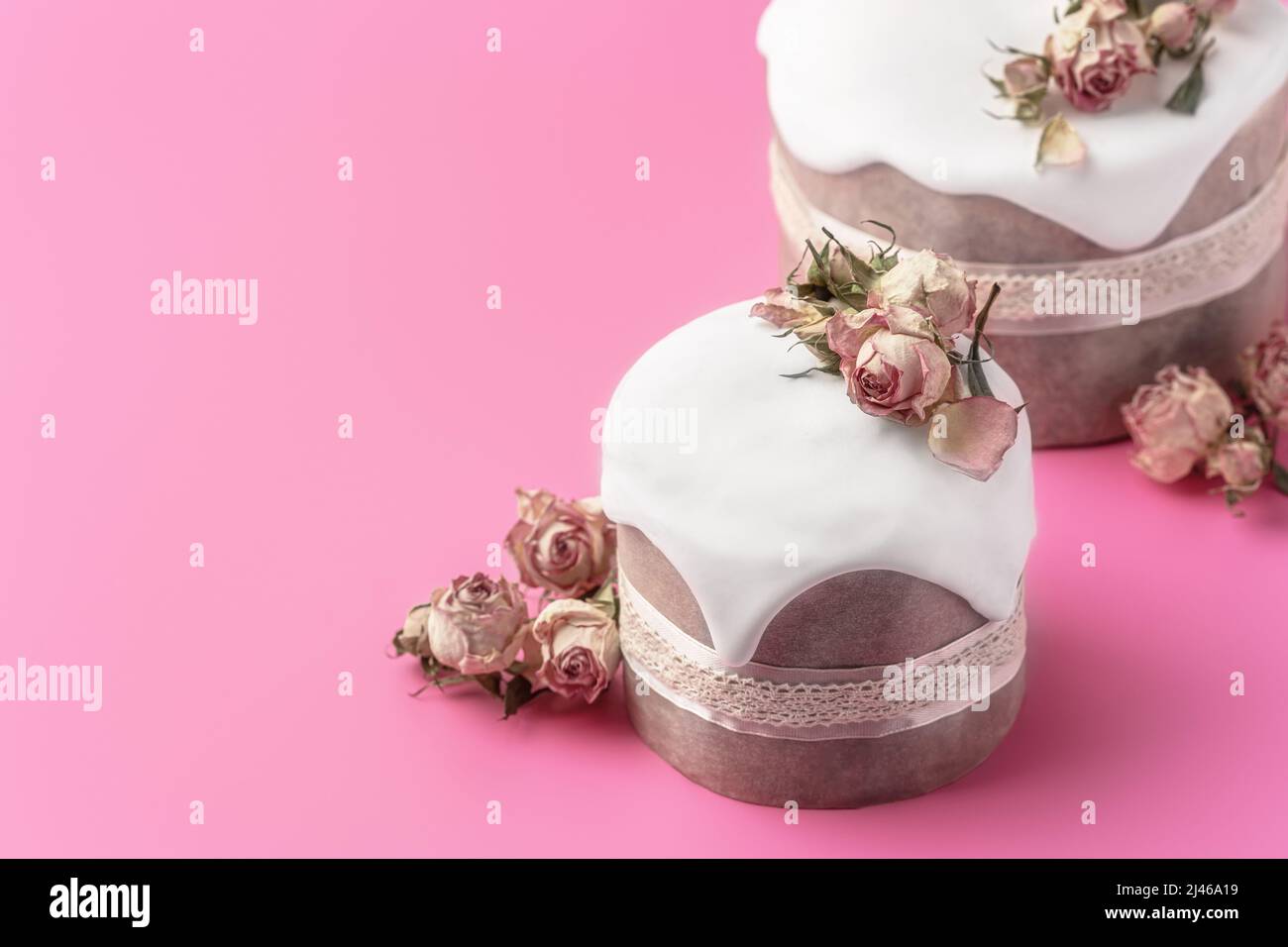 Gâteaux de Pâques vitrés décorés de fleurs de rose de thé sur fond rose vif. Composition de Pâques avec gâteaux, roses et œufs au chocolat. Arrière-plan de Pâques avec espace de copie pour votre conception. Banque D'Images