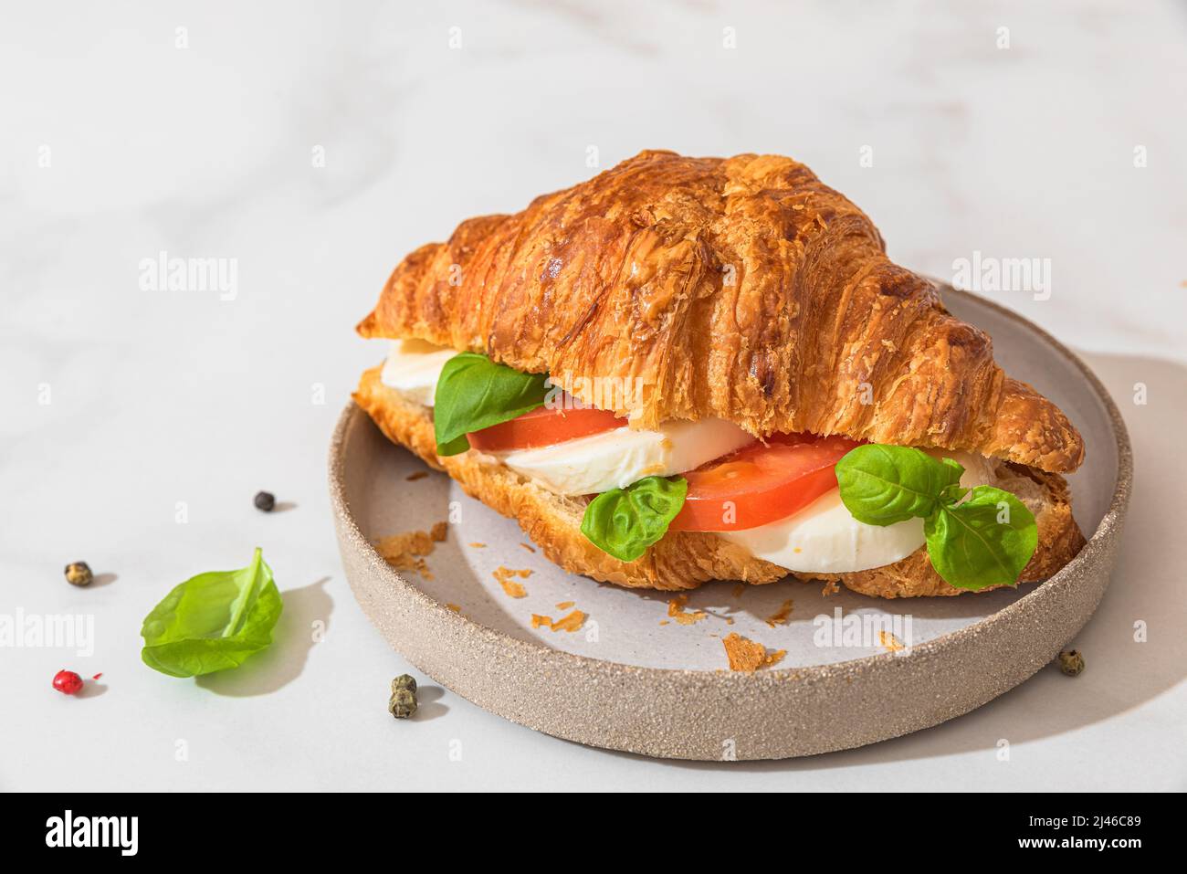 Sandwich croissant avec mozzarella, tomate et basilic dans une assiette sur fond blanc. Petit déjeuner italien. Nourriture savoureuse Banque D'Images
