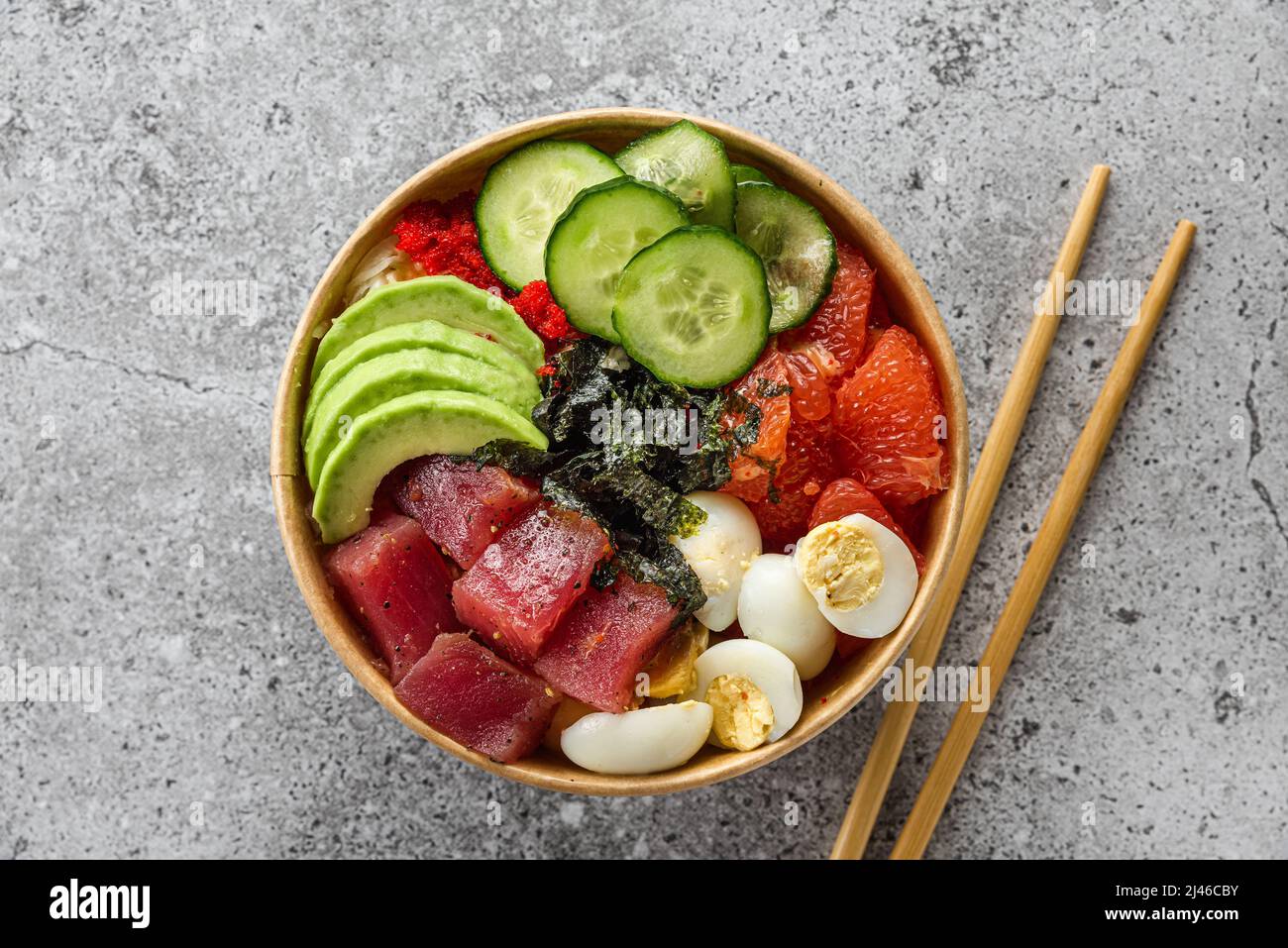 Boîte en papier ou paquet avec salade de thon à l'avocat à emporter ou livraison de nourriture avec baguettes sur fond gris. Vue du dessus. Une alimentation saine Banque D'Images