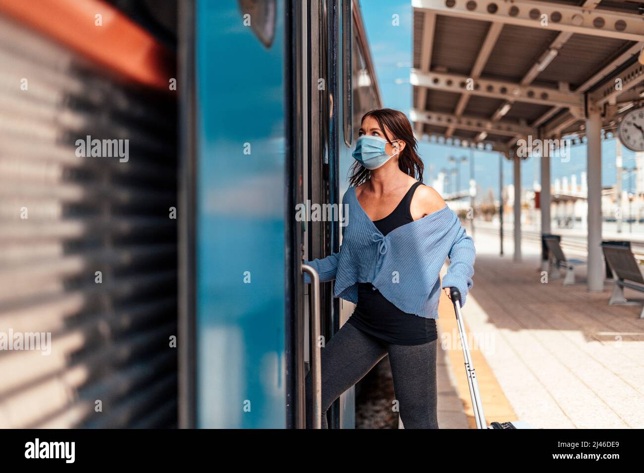 Une jeune femme en masque de protection se trouvant dans le train avec un bagage Banque D'Images