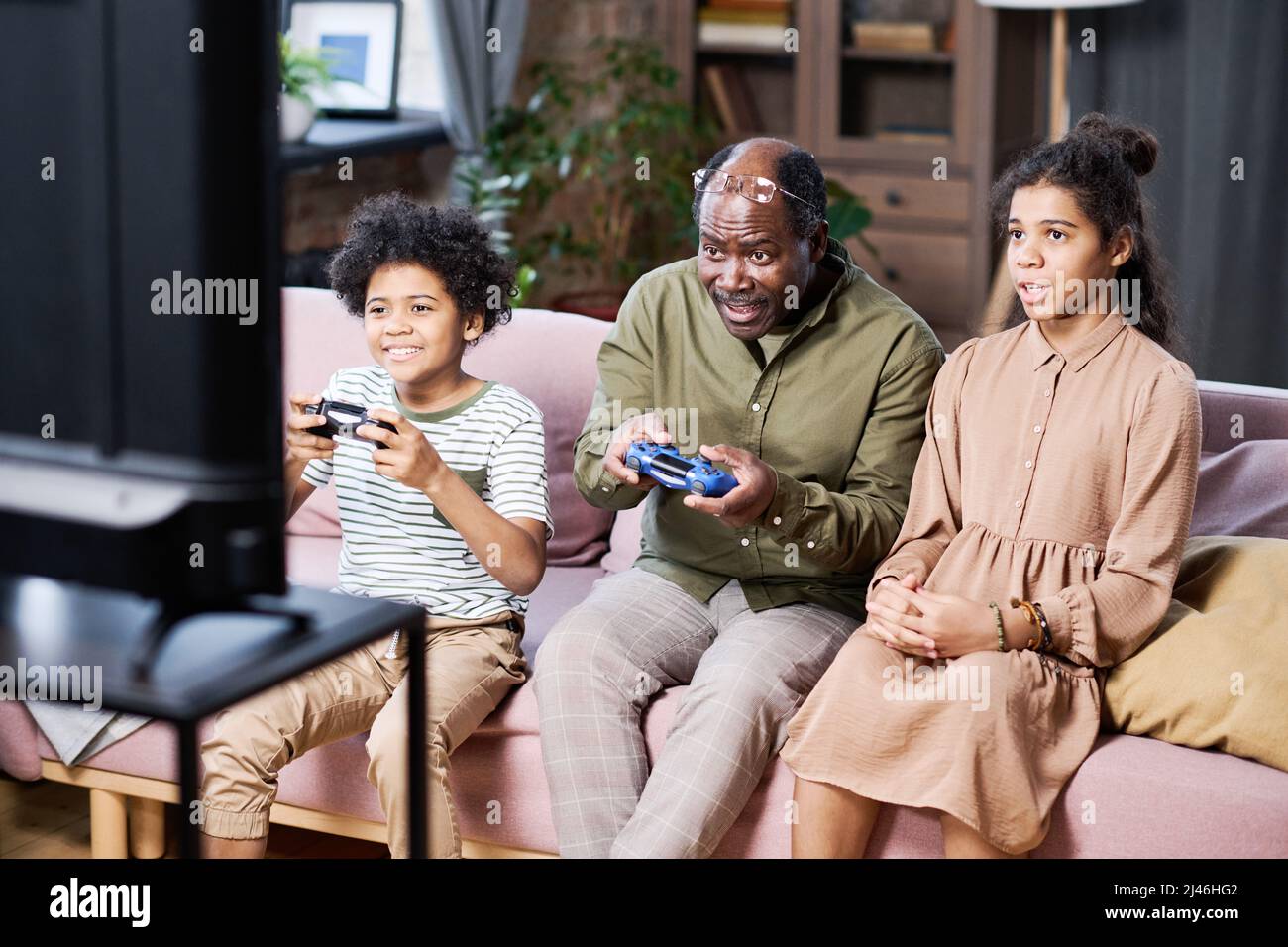 Groupe de petits-enfants heureux et leur grand-père jouant des jeux de loisirs devant le téléviseur tout en étant assis sur un canapé dans le salon Banque D'Images