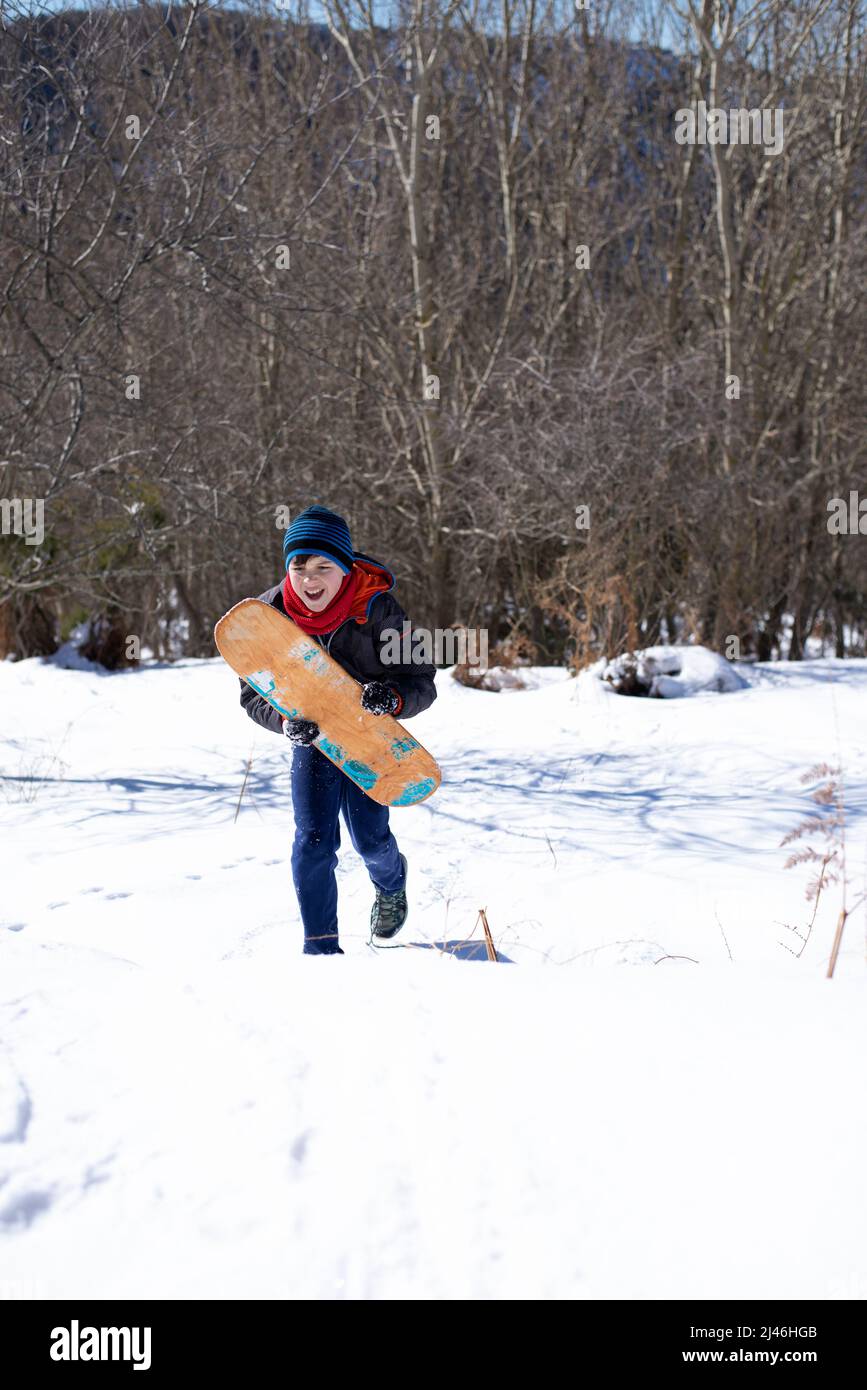 Joyeux adolescent homme courir sur la neige tout en tenant un surf Board Banque D'Images