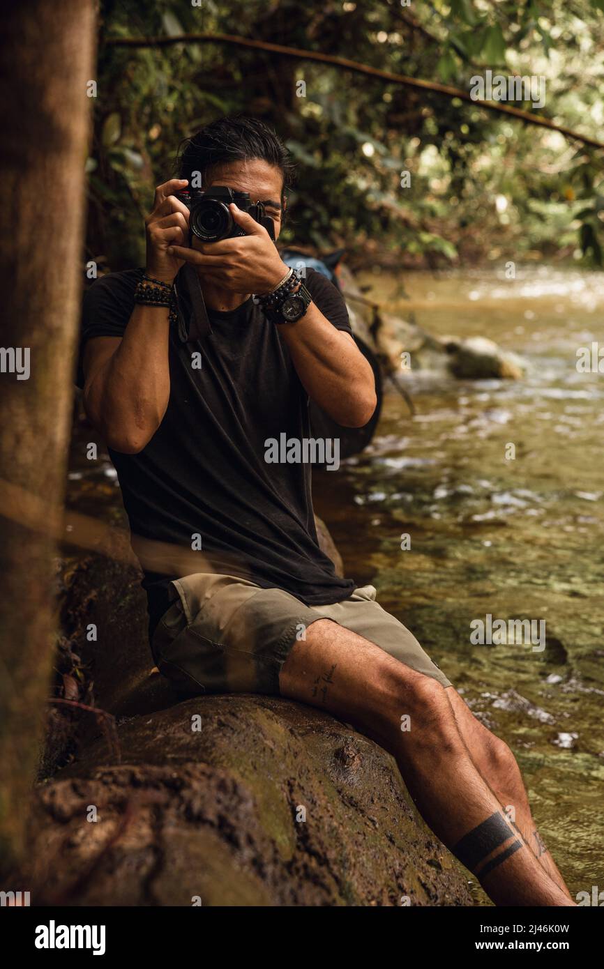Homme assis sur un arbre prenant des photos avec son appareil photo professionnel Banque D'Images