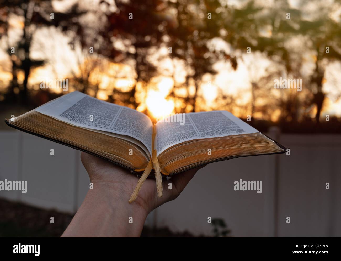 Gros plan femme dépassant la main avec la Bible ouverte près de coucher de soleil lumineux dans l'arrière-plan. Espace de copie. Banque D'Images