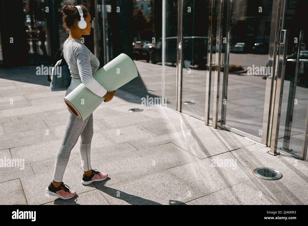 Femme sportive de yoga en tenue active et casque de marche avec tapis pour l'entraînement Banque D'Images
