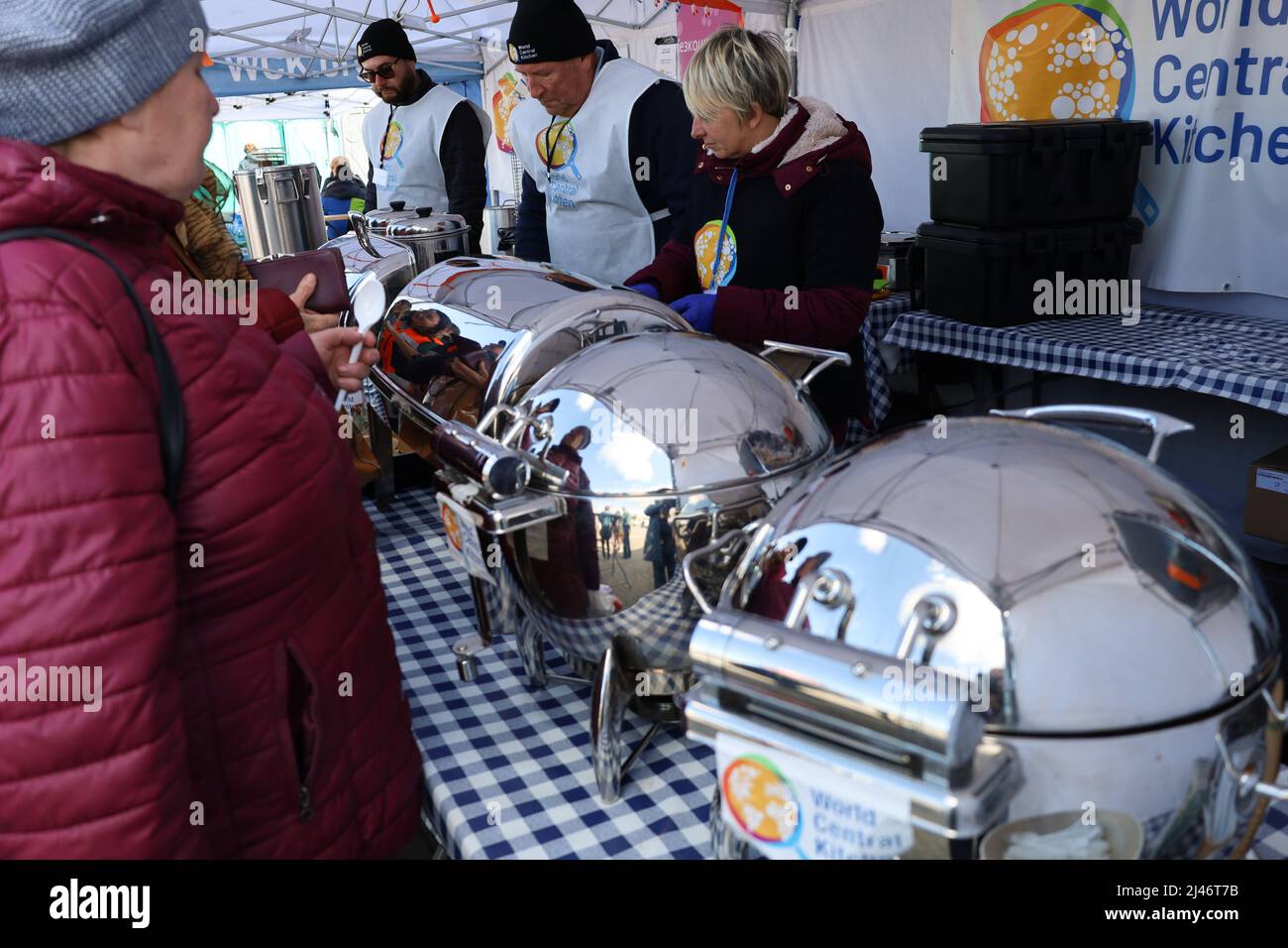 Przemysl, Pologne. 12th avril 2022. Les réfugiés ukrainiens reflétés dans le conteneur de service en métal reçoivent un délicieux ragoût de bœuf chaud pour le déjeuner à la tente de World Central Kitchen à Tesco. Les réfugiés passent par Tesco, l'un des principaux centres humanitaires pour les réfugiés ukrainiens près de la frontière entre l'Ukraine et la Pologne. Ils sont récemment arrivés en Pologne après avoir fui la terreur de Poutine en Ukraine. (Image de crédit : © Amy Katz/ZUMA Press Wire) Banque D'Images