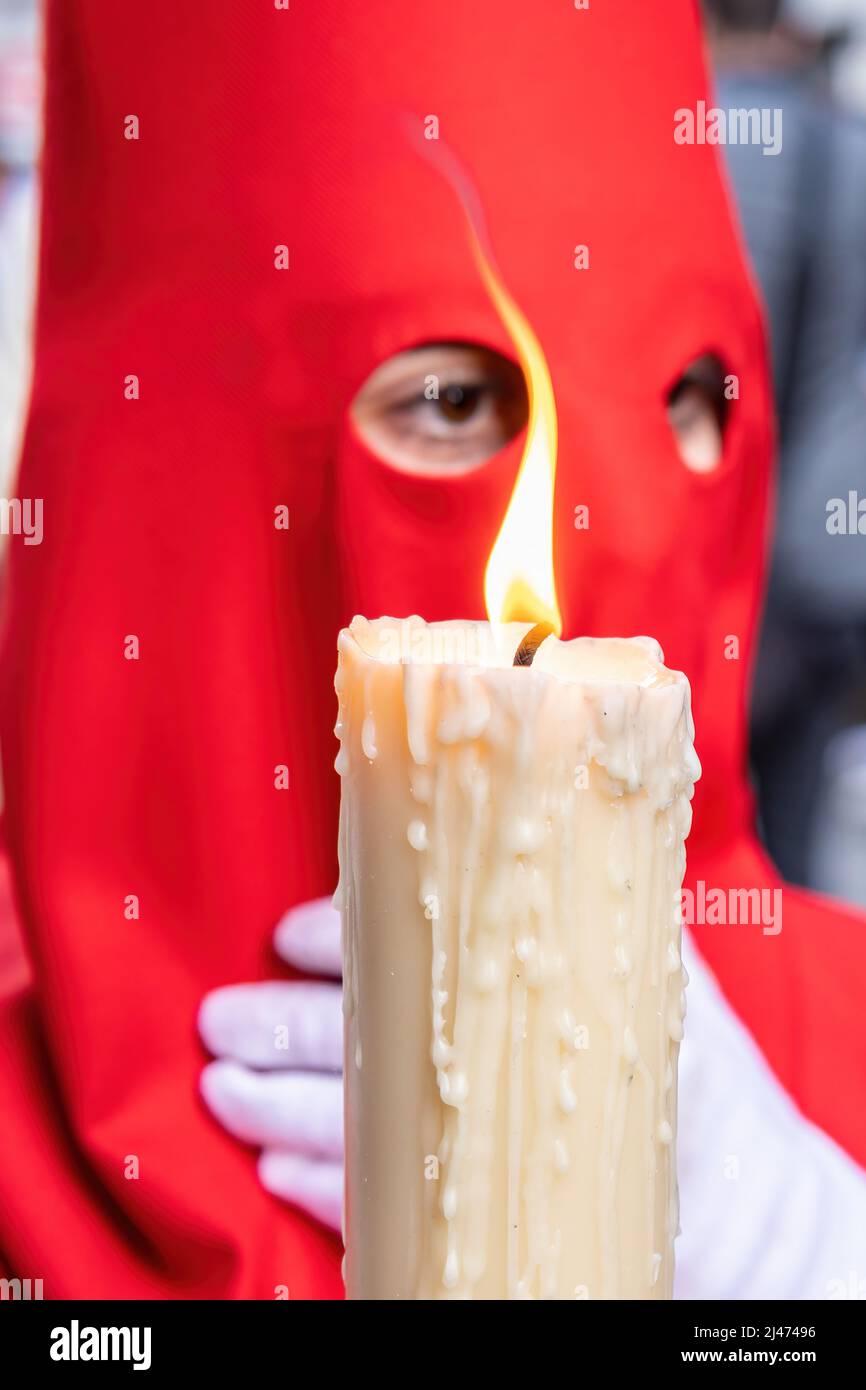 La bougie en flamme d'un jeune Nazaréen avec une cagoule rouge faisant sa station de pénitence dans la procession de la semaine Sainte. Mise au point sélective avec flamme seulement Banque D'Images