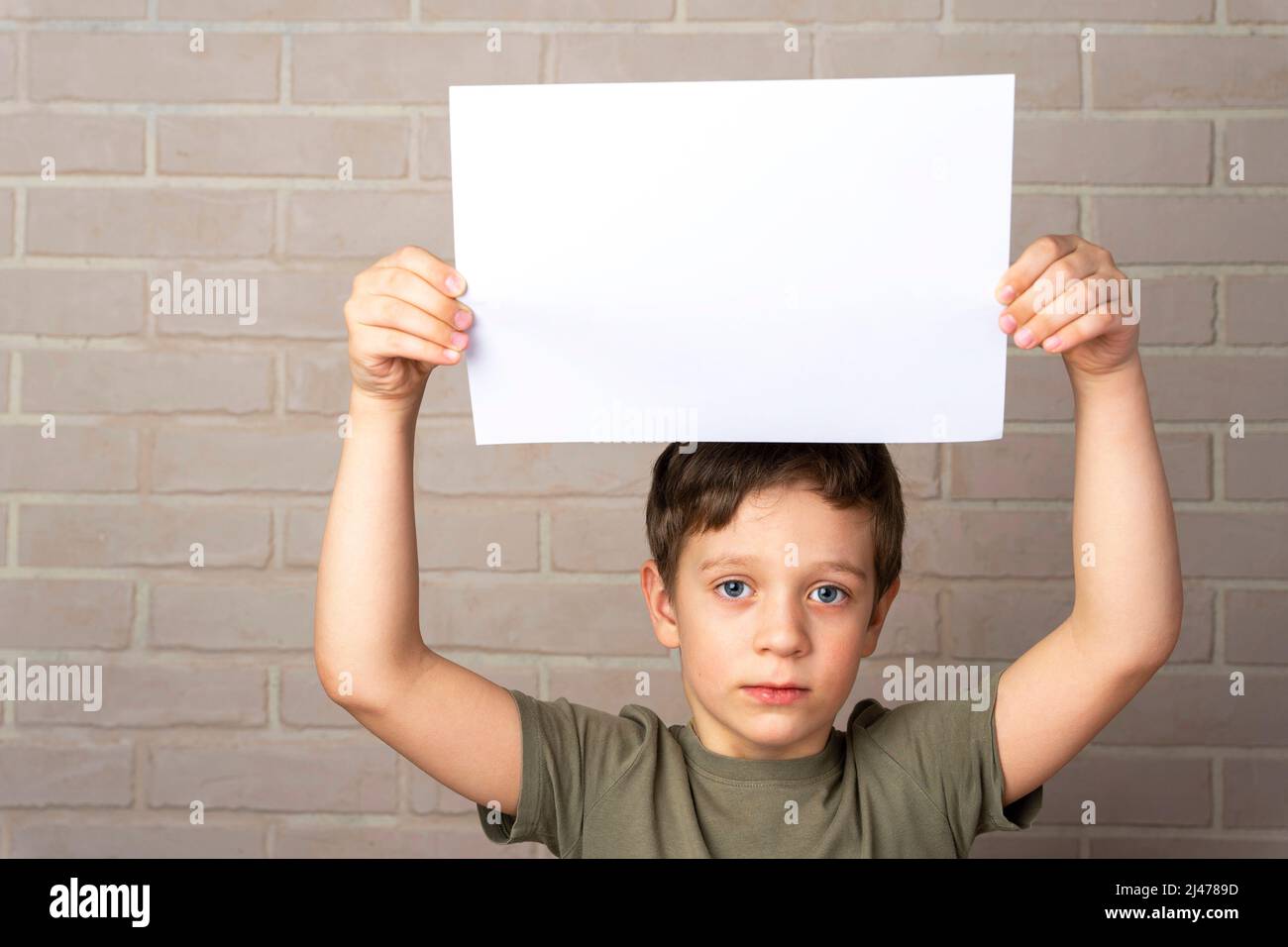 Un garçon européen sérieux de 5 ans tient une affiche vide au-dessus de sa tête. Banque D'Images