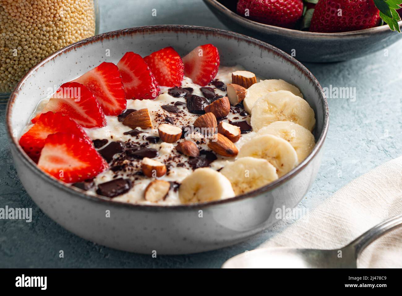 Porridge de millet avec fraise, banane, morceaux de chocolat noir, noisette et amande dans un bol en céramique Banque D'Images