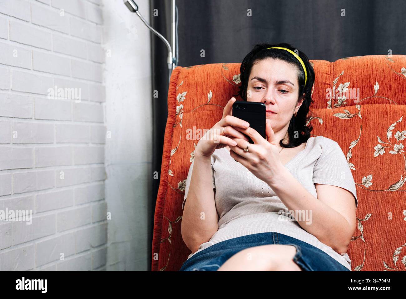 Une femme d'âge moyen est assise sur le canapé et utilise un smartphone Banque D'Images