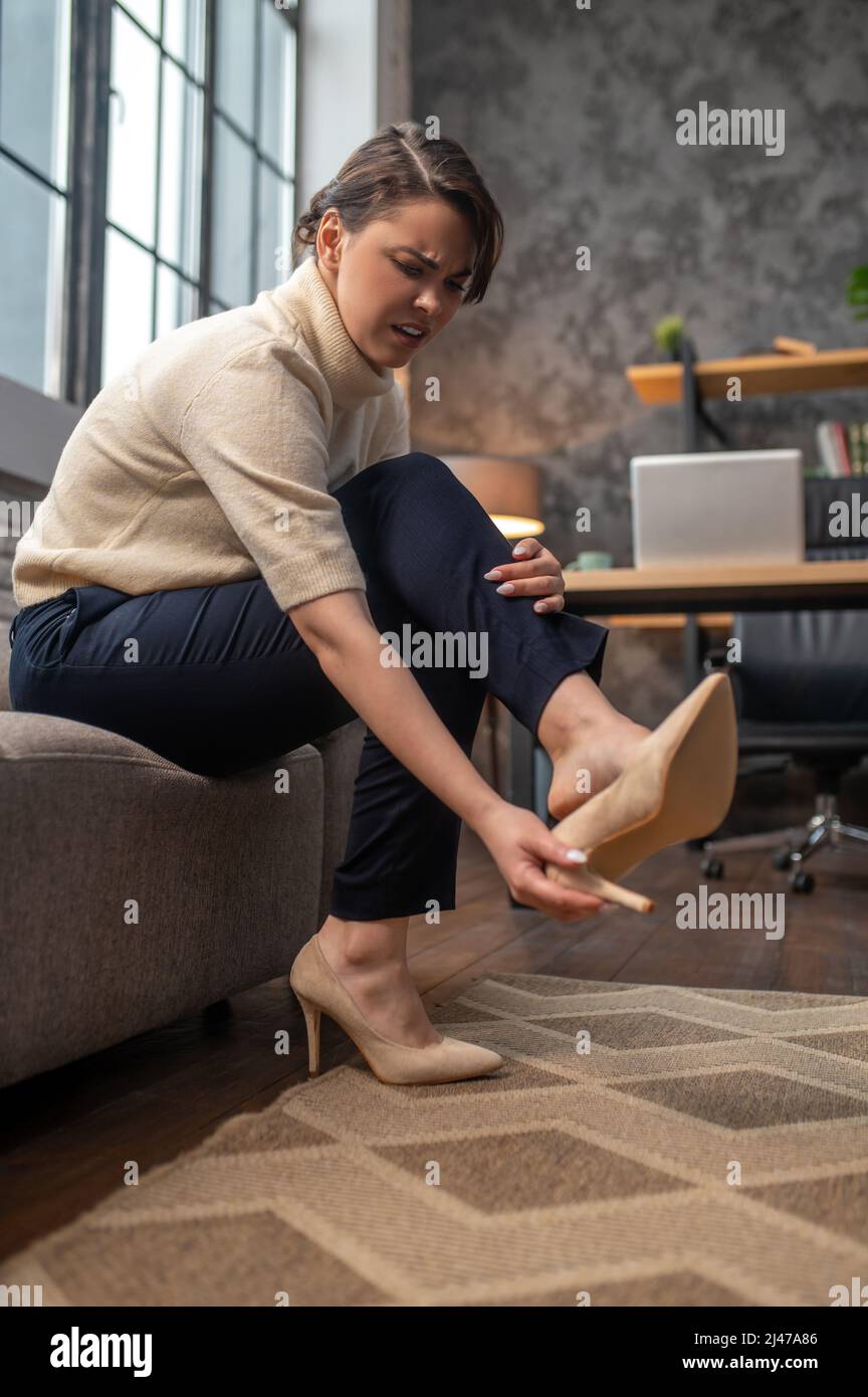 Une femme qui prend des chaussures sur des talons hauts après une longue journée Banque D'Images