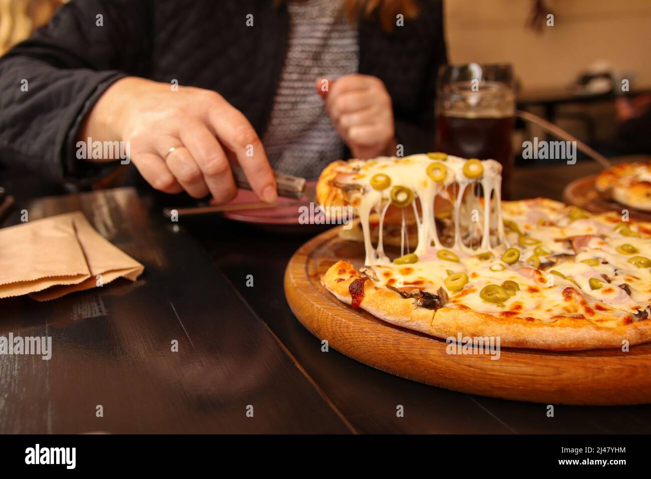 Défpoint main femelle tenant une tranche de pizza italienne tortilla avec Mozzarella râpé. Pizza aux olives, basilic et fromage en gros plan. Pizzeria à l'extérieur. Ou Banque D'Images