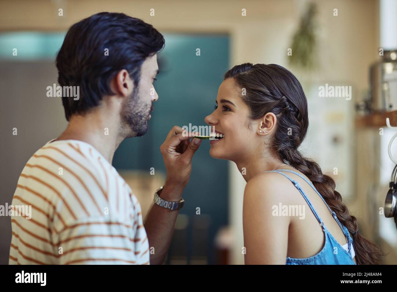 L'amour rend tout le goût meilleur. Photo d'un jeune couple affectueux qui se grignote tout en préparant un repas dans sa cuisine. Banque D'Images