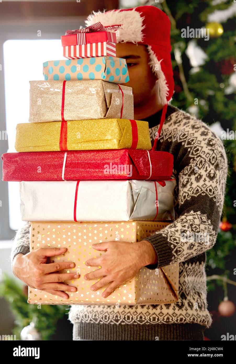 Si Noël n'est pas trouvé dans votre coeur, vous ne le trouverez pas sous un arbre. Photo d'un jeune homme portant une pile de cadeaux à la maison. Banque D'Images