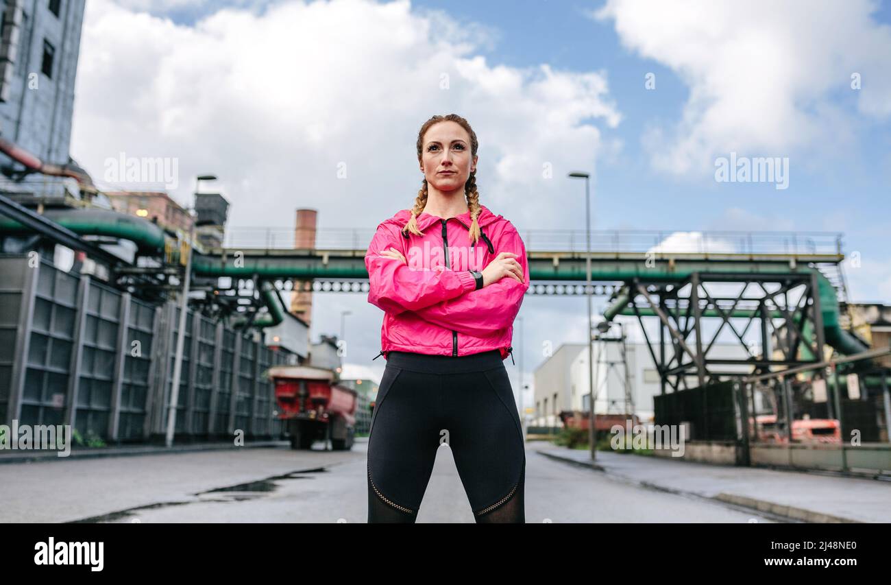 Sportswoman avec bras croisés posant devant une usine Banque D'Images