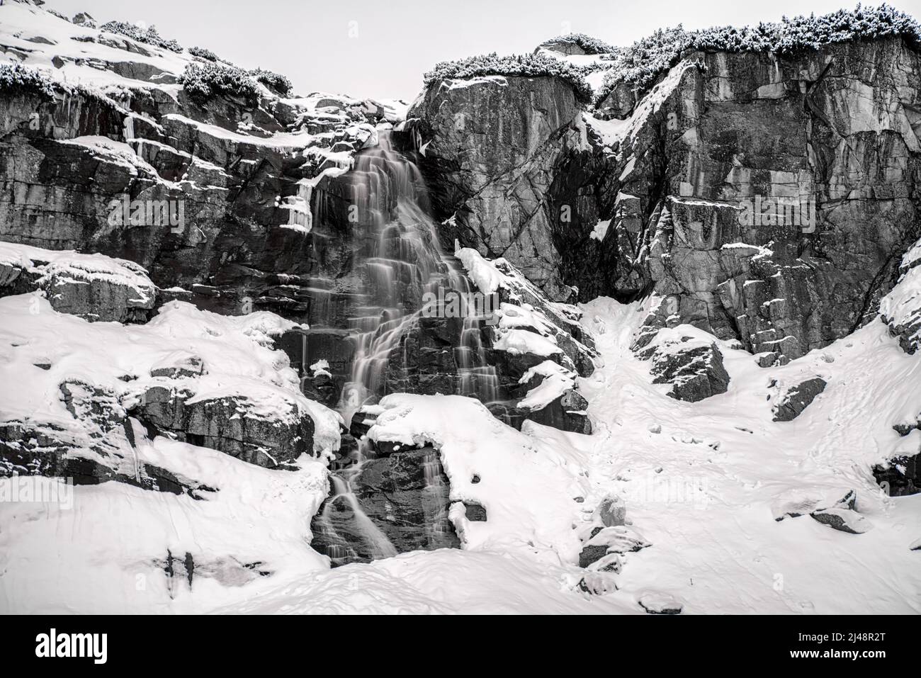 Plan d'eau à longue exposition en montagne en hiver. Photographie en noir et blanc. Cascade Skok dans les montagnes de Tatras, Slovaquie. Banque D'Images