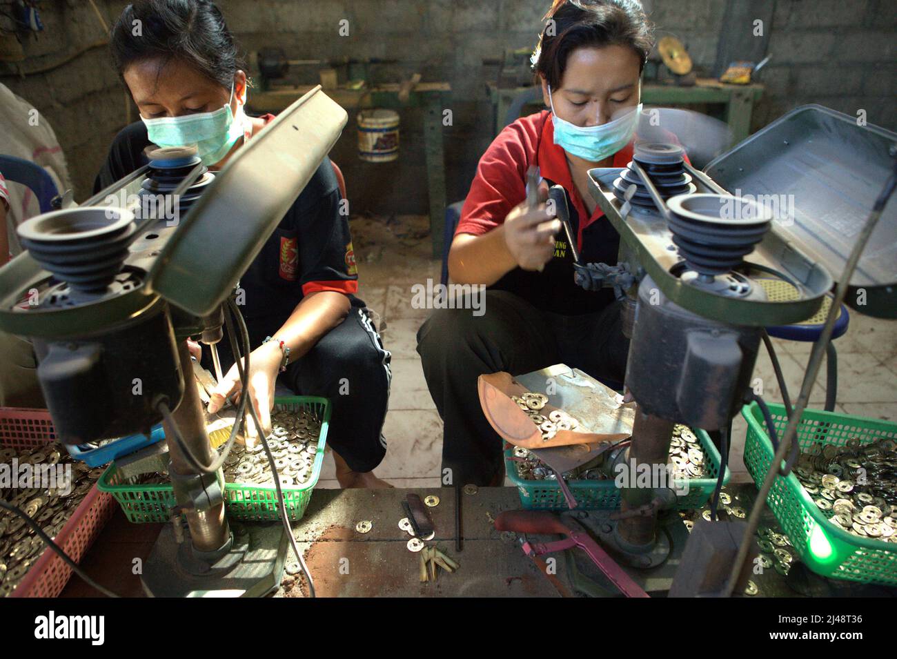 Femmes travaillant dans une usine produisant des pièces de monnaie balinaises traditionnelles avec un creux connu sous le nom de 'pis bolong/jinah bolong/uang kepeng' dans le village de Kamasan, Klungkung, Bali, Indonésie. Utilisées dans les transactions à travers Bali dans le passé, les pièces sont aujourd'hui essentielles dans les rituels religieux traditionnels de l'île des dieux. Banque D'Images