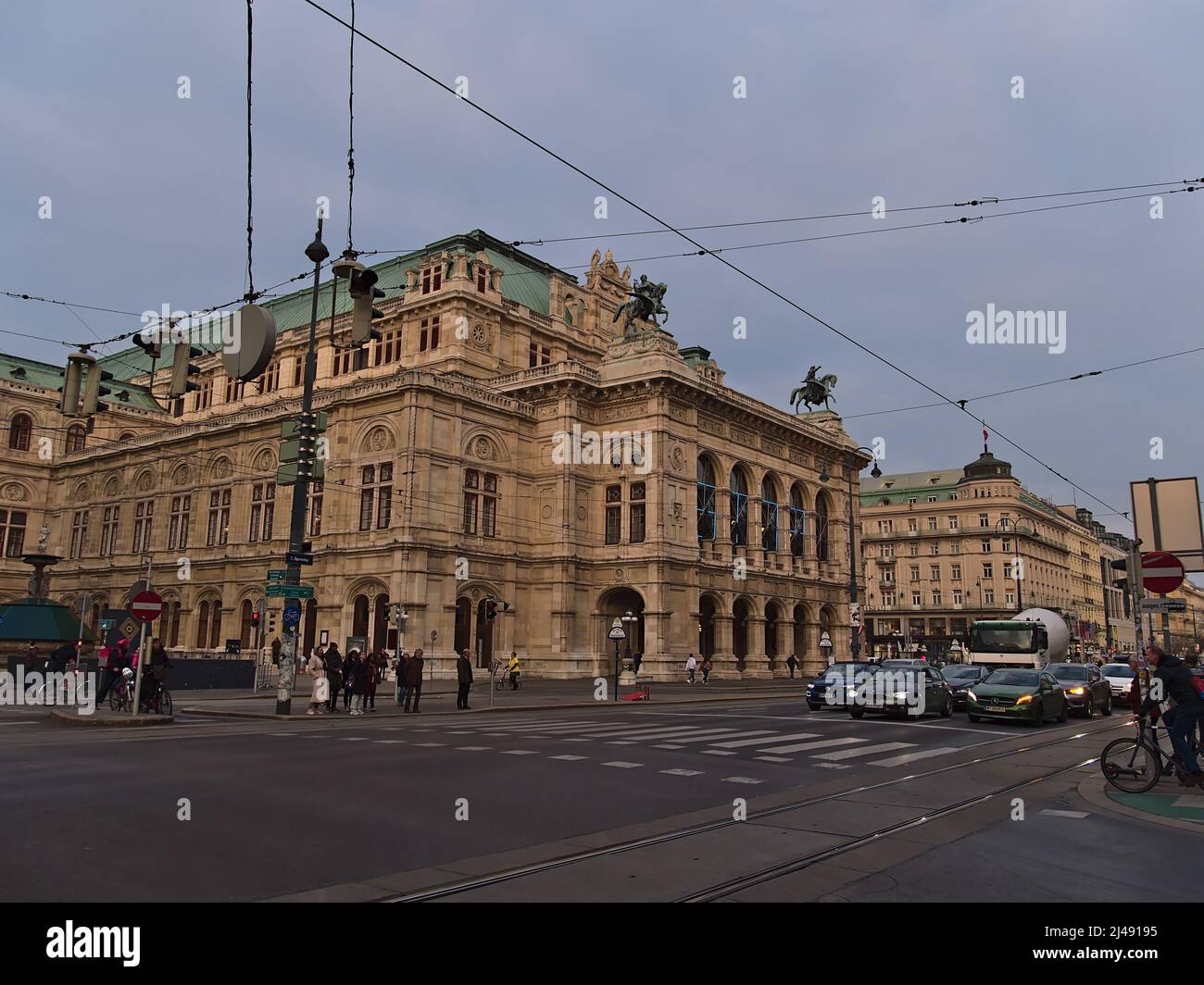 Vue sur le bâtiment historique du célèbre Opéra d'Etat de Vienne en Autriche par une journée nuageuse le soir avec des voitures et des personnes en face. Banque D'Images