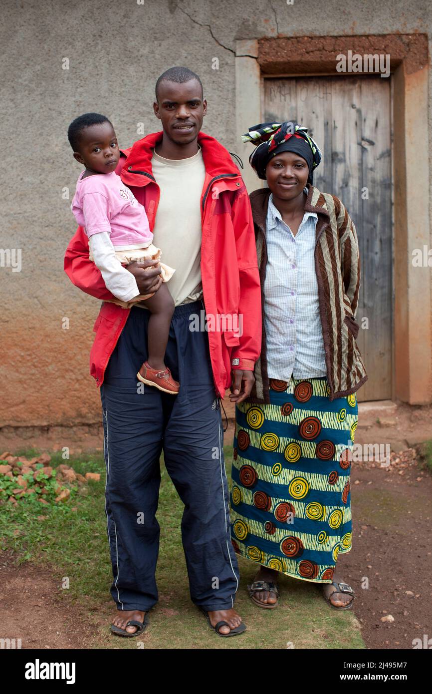Thacien Kalinda, 24 ans, avec son épouse Chantal Nyiraneza, 24 ans, et son bébé Gisele Uwase à l'extérieur de sa maison familiale. Sa famille s'est enfui au Congo en 1994 quand il avait 7 ans. Il était séparé de ses parents et de sept frères et sœurs qu'il n'a jamais vus depuis. Il était avec une tante qui l'a ramené à la maison 1996. Elle est morte lorsqu'il avait 18 ans au primaire en 6 et qu'il a abandonné l'école parce qu'il ne pouvait pas payer les frais d'école. Il a vécu comme un garçon de rue jusqu'à ce qu'il s'implique dans le programme. À la suite du projet, il a été en mesure de cultiver la terre qu'il a hérité de son père, payer 300 000 fra Banque D'Images
