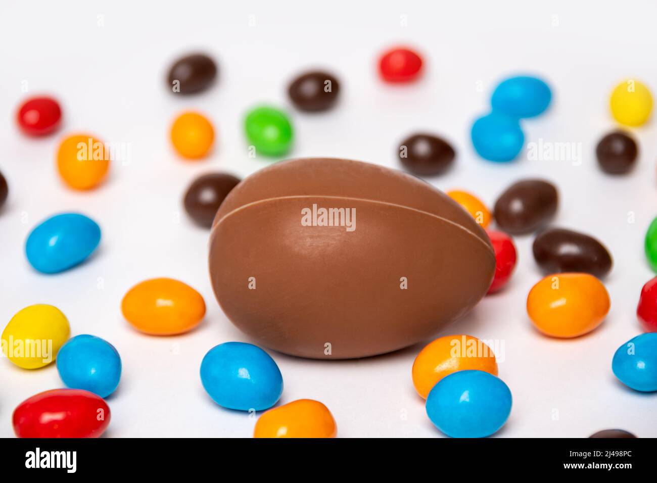 Un œuf de chocolat entier sur fond blanc avec des bonbons colorés. Gâteries pour enfants. Dessert sucré pour les enfants. Douce tradition de Pâques. Banque D'Images