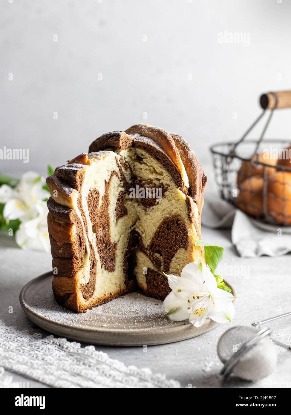 Gâteau de Pâques ciré kraffin arrosé de sucre en poudre et d'une fleur blanche sur une assiette . Gros plan sur un gâteau fait maison en deux couleurs. Cruffin. Vertica ou Banque D'Images