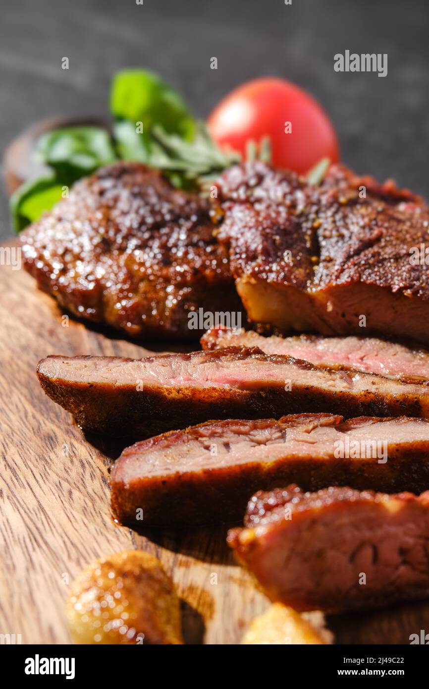 Vue rapprochée de l'araignée de beefsteak frite dans une poêle en fonte, servie sur un plan de coupe en bois avec tomate et basilic Banque D'Images