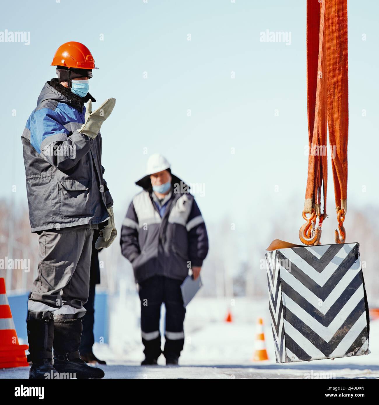 L'ingénieur passe l'examen du slinger. Mouvements de l'opérateur pour soulever la charge de commande. Formation des slingers. Scène authentique du processus de travail en hiver dans la rue. Banque D'Images