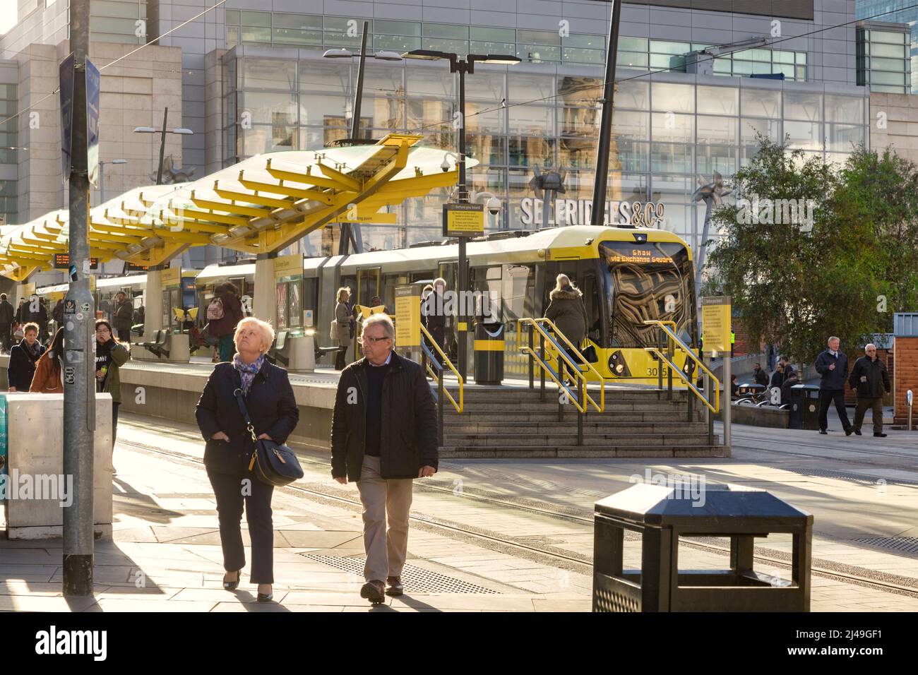 2 novembre 2018 : Manchester, Royaume-Uni - Arrêt de tramway Metrolink à Exchange Square, couple senior à pied, soleil d'hiver. Banque D'Images