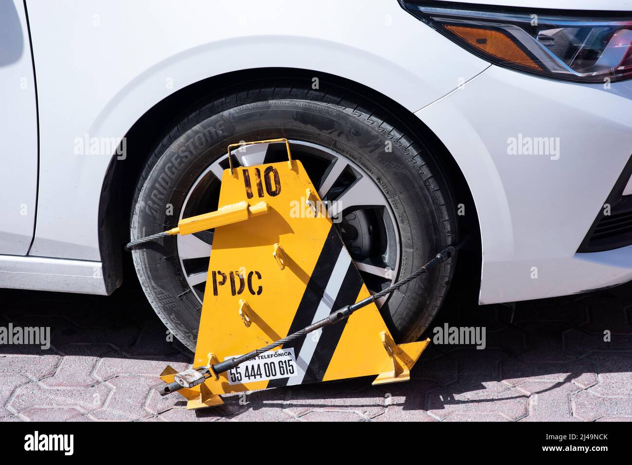 Gros plan d'une roue de voiture blanche bloquée par un blocage de roue en raison d'une violation de stationnement illégale. Mise au point sélective. Banque D'Images