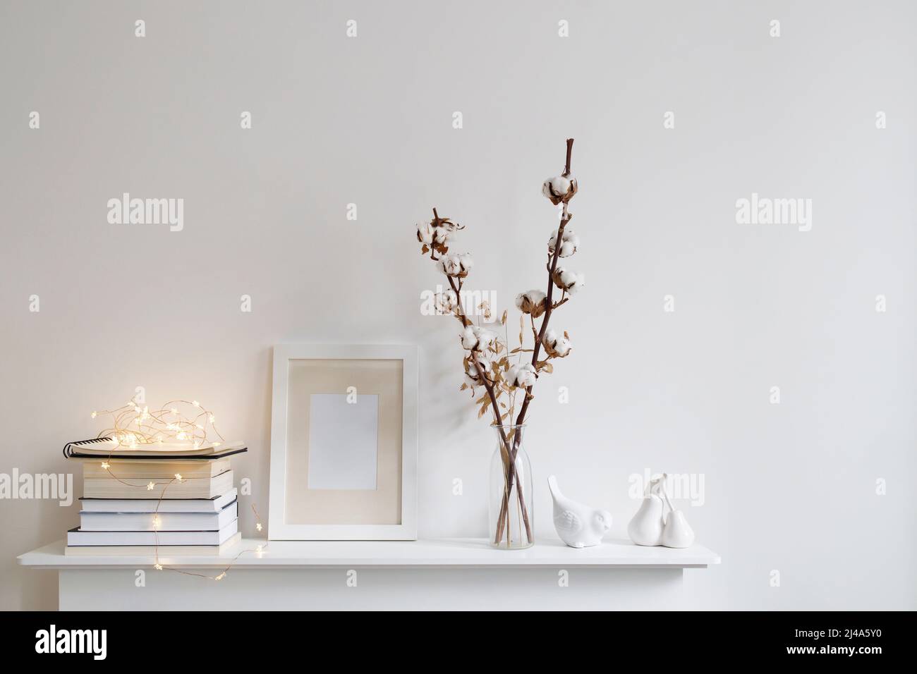 Décoration de style scandinave dans des tons blancs. Un vase avec des fleurs de coton, une pile de livres, un cadre photo, une figurine d'oiseau sur une surface en bois d'un Banque D'Images