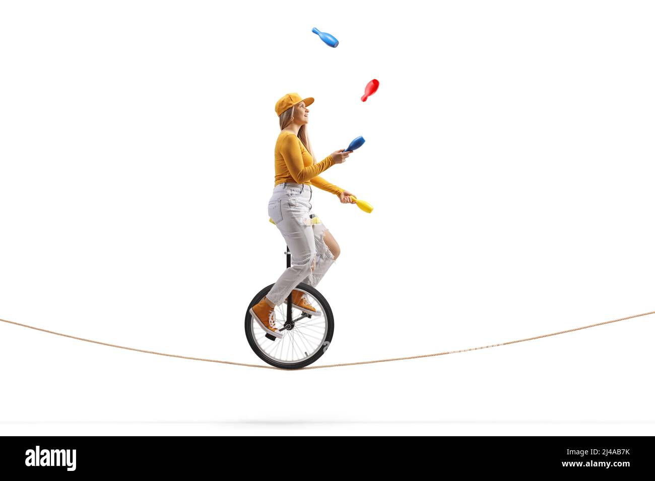 Jeune femme à cheval sur un monocycle sur une corde raide et à jongler isolée sur fond blanc Banque D'Images