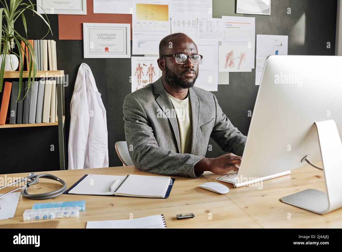 Un homme africain médecin assis sur son lieu de travail au bureau et travaillant sur un ordinateur Banque D'Images