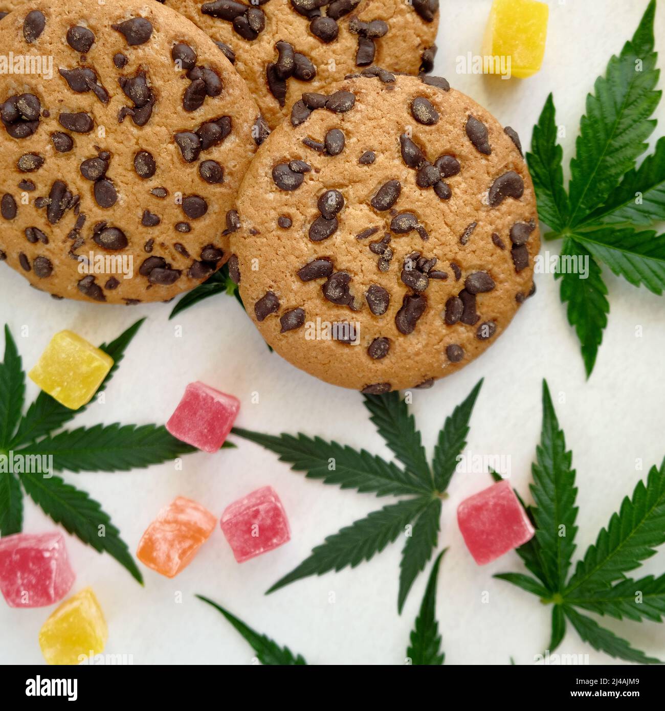 Biscuits américains avec extrait de cannabis. Bonbons à l'huile CBD. Feuilles de marijuana sur fond blanc. Vue de dessus, plan d'appartement. Banque D'Images