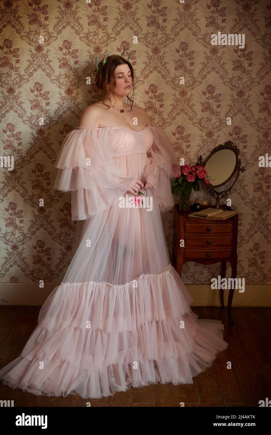 Jeune femme en posture romantique portant une robe poudreuse rose dans un décor vintage Banque D'Images