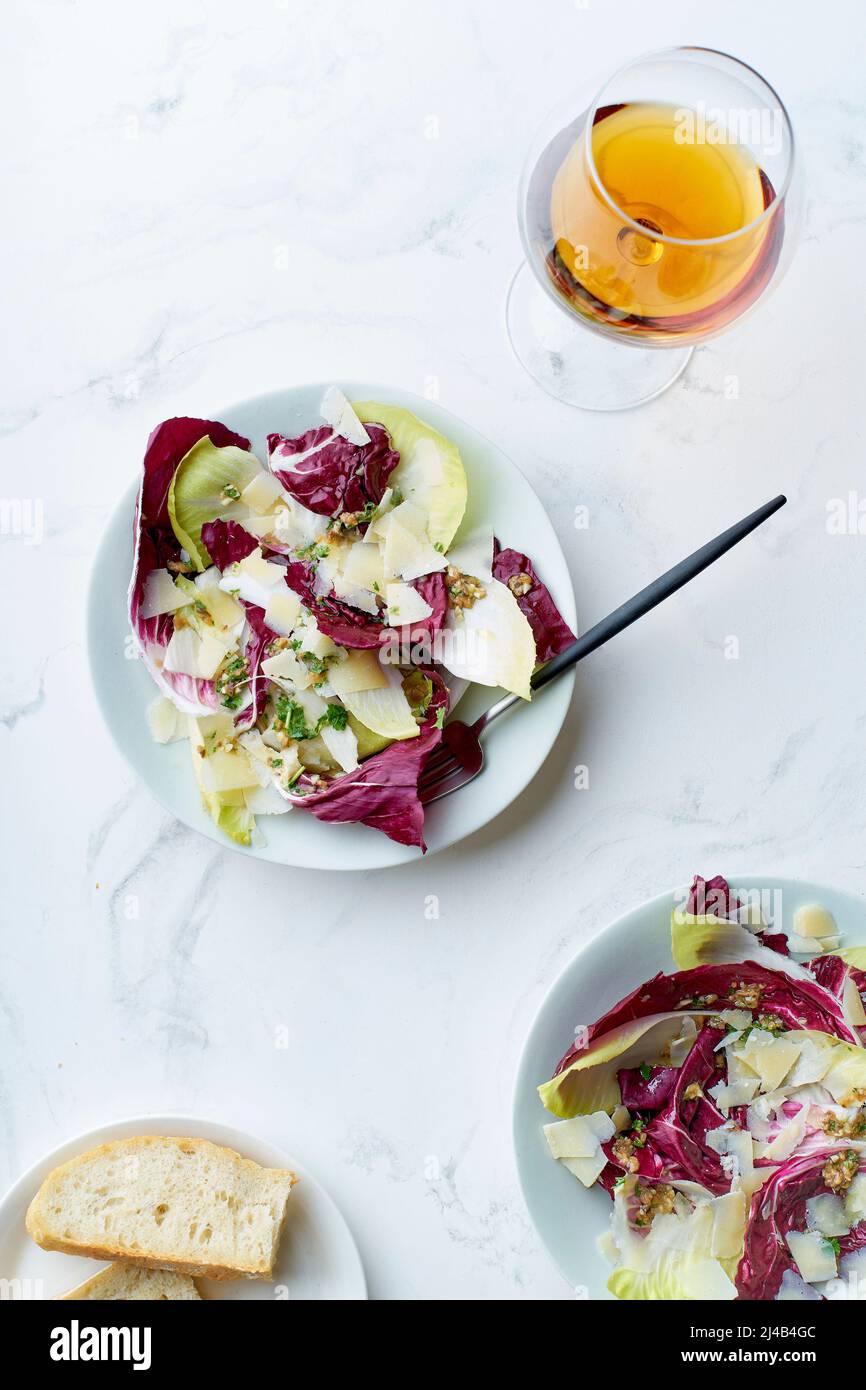 Salade au radicchio, chicorée et parmesan servie avec un verre de vin orange sur fond blanc Banque D'Images