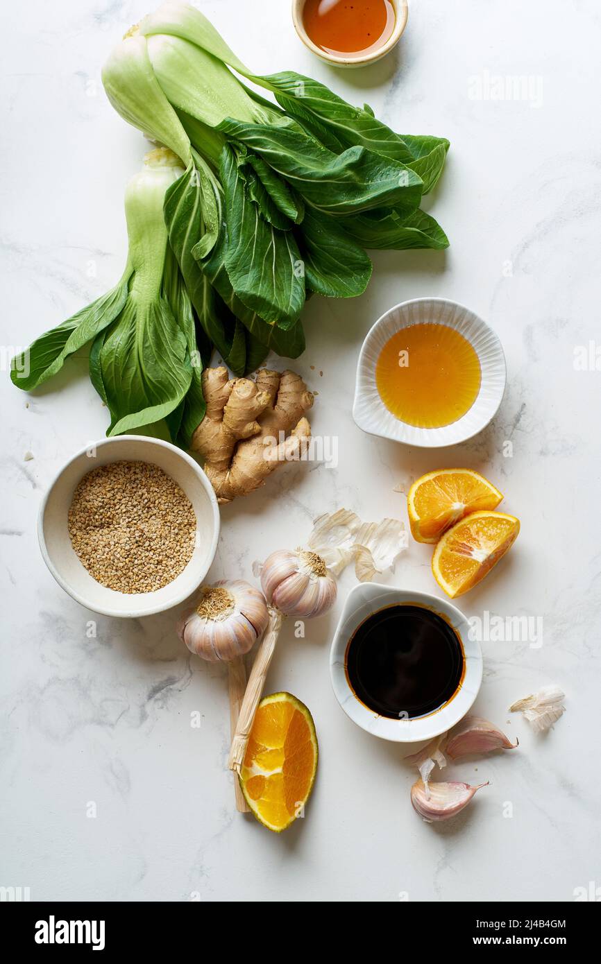 Ingrédients pour cuisiner un plat de cuisine asiatique sur une table en marbre. Bok choy frais, tranches d'orange et condiments. Banque D'Images